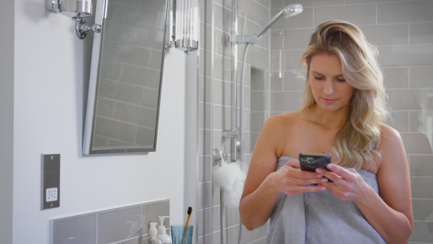Mature woman getting ready in bathroom at home looking at mobile phone and laughing - shot in slow motion