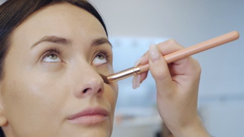 Close-up of the hand of the make-up artist makes the model's makeup and removes bags under the eyes. Concealer under the eyes. Beauty industry