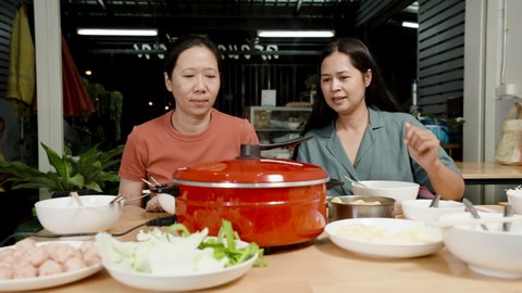 4K slow-motion, an Asian female best friend wearing brown and green shirts is excited about sukiyaki in a red pot that is about to be cooked and ready to eat.