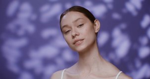Beautiful young Caucasian model without makeup, with tied hair, smiling broadly looking into the camera while standing against the background of falling rose petals in the studio. 4K video, red komodo