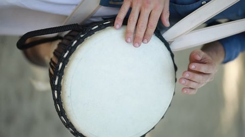 A European man plays the Djembe drum, holding it between his legs. A European man plays the Darbuka instrument. Caucasian man playing african djembe drum. Vertical video. Slow motion