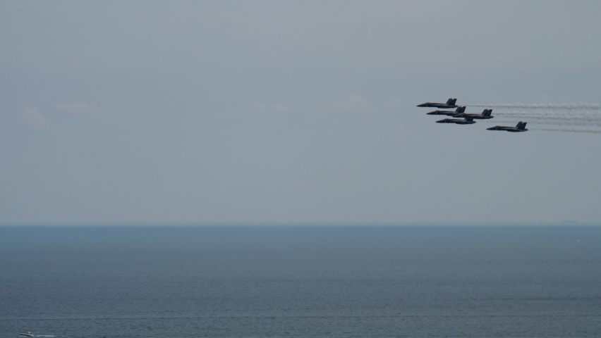 Fighter jets in tight formation fly over Lake Michigan and many sail boats on a sunny summer day in 2021. Jets disappear behind a wall of skyscrapers