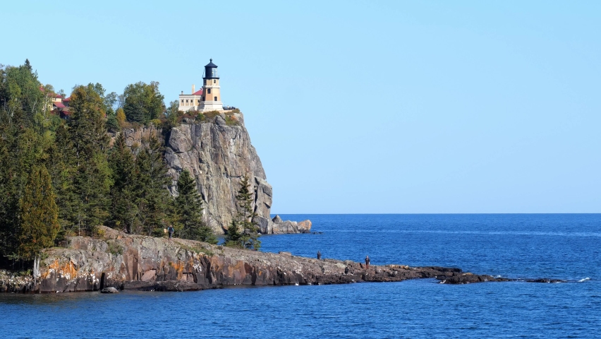 People enjoying Split Rock Light House on the north shore of Lake Superior in Minnesota. A rocky cliff and outcrop along the beautiful blue water of gitchi-gami, a popular travel destination.
