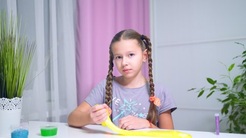 girls playing with yellow shiny slime at the table at home