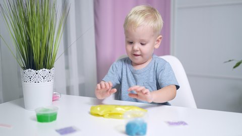little boy blond playing with yellow shiny slime at the table at home