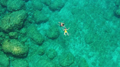 Aerial view of a young couple snorkeling above coral reef reaching deeper parts of the crystal clear water, Rhodes, Greece. Aerial drone view of a couple snorkeling swimming in crystal clear water.