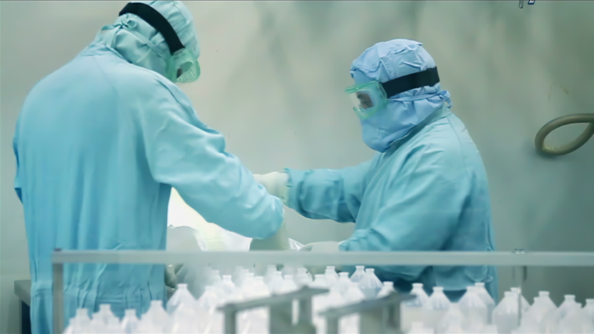 Two Men Wearing Bio Hazard Gear Working in the Production Line at a Pharmaceutical Plant. 4K Resolution. Royalty-Free Stock Footage #1085005081