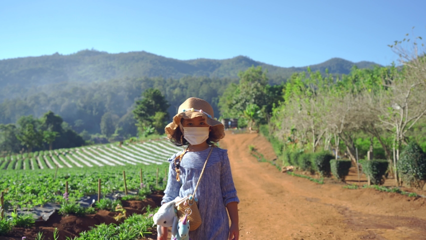 Cute small girl with protective face mask walking at strawberry farm.