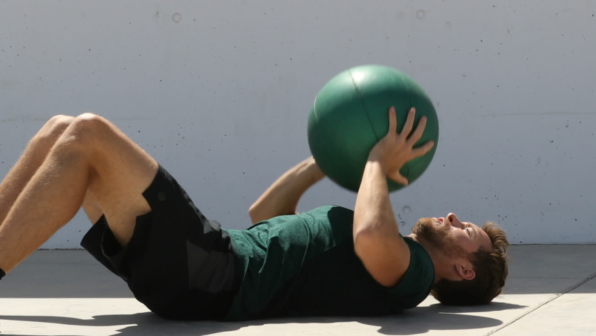 Fitness man. Strength training fit man cross training throwing medicine ball in the air for bench press arm workout exercises using heavy weight ball. Fitness athlete exercising on gym floor