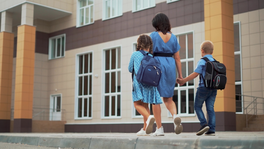 Happy family back to school. Mom and children go to school in schoolyard. Children with backpacks hold their mother hand. Happy family mom and children go to school. Family walks through schoolyard Royalty-Free Stock Footage #1085008633