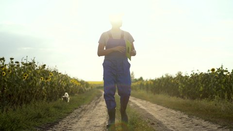 Agriculture. Farmer in rubber boots walks along a rural road. Agricultural business. Farmer in field. Agriculture concept. Farmer walk along rural road in green field. Agricultural business concept