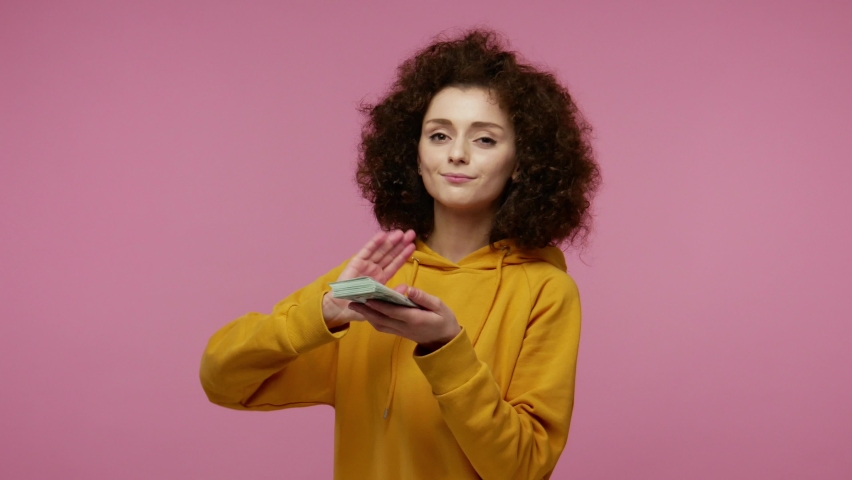 Wasteful girl afro hairstyle in hoodie scattering dollars looking arrogant, boasting wealthy life, concept of careless money spending, squandering throwing around cash. indoor studio shot isolated Royalty-Free Stock Footage #1085009086