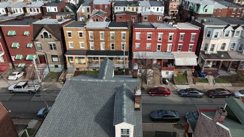 People walk on sidewalk street by houses in urban American city. Aerial establishing shot.