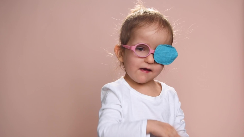 Baby girl 3 years old wearing glasses and an occluder  to prevent astigmatism, amblyopia and strabismus (squint, lazy eye). She is happy. Royalty-Free Stock Footage #1085012740