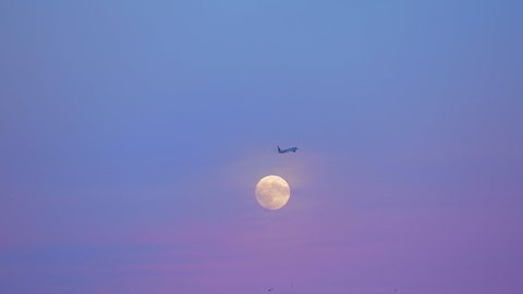 airplane in flight at night very peri pantone sky colors passing full moon