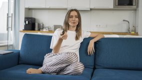 A young woman sitting on a sofa with a TV remote control and switching channels, front view - Powered by Shutterstock - Get 15% off with code: PIKWIZARD15