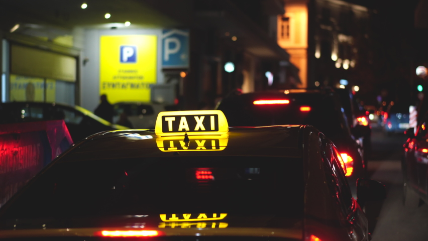 Close-up view on LED illuminated lights of TAXI sign on top of cab car. Driver stopped, waits for passengers, clients. Late evening hours service. Yellow color neon glowing. Twilight city streets taxi Royalty-Free Stock Footage #1085021749