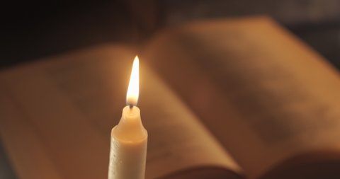 A Burning Candle and an Old Book. Reading and teaching by candlelight at night.