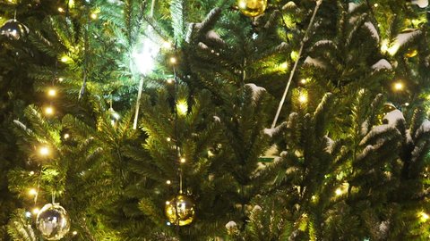 Close up a Christmas tree lights glittering at night. New Year fir tree with decorations and illumination. Xmas tree decorations background. Many large golden balls on fir tree New Year and Christmas.