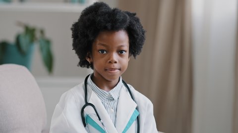 Close-up african american little girl standing in medical clothes playing pretending to be doctor charming child looking at camera smiling shows OK sign gesture no problem future professions concept