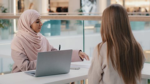 Two young girls sitting at table friendly muslim woman financial advisor explaining benefits contract manager sales agent lawyer consults with client business meeting legal consultation negotiation