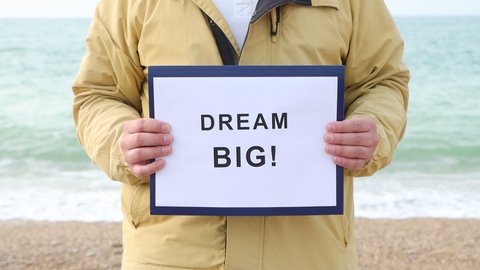 Man holds poster with words DREAM BIG! Motivational concept footage.