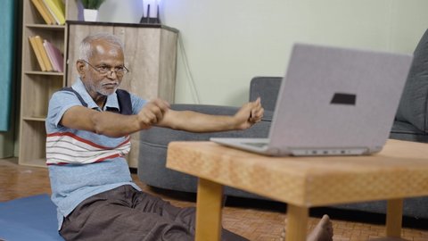 senior man doing excerise by watching online yoga videos on laptop at home - concept of online fitness training, technology and healthy lifestyle during coronavirus or covid-19 pandemic lockdown.