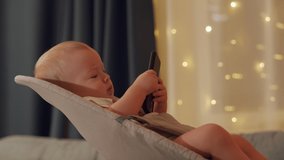 Cute little child using mobile device, baby boy watching movie on TV and using smart phone at same time. High quality 4k footage
