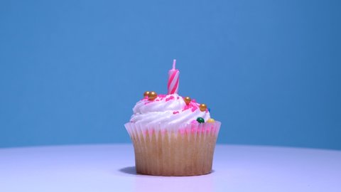 Lighting birthday candle on cupcake, closeup. Delicious sweet cup cake with burning candle on pink background. Homemade vanilla muffin with buttercream frosting. Shallow depth of field.