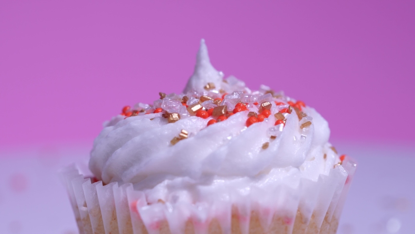 Cupcake macro shallow depth of field view. Decorated sugar sprinkles cup cake with white vanilla cream on pink background. Delicious desserts muffin for girl birthday or Valentine day.