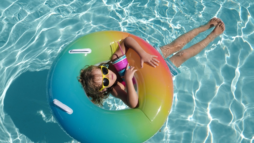 Happy kid playing with colorful swim ring in swimming pool on summer day. Child water toys. Children play in tropical resort. Family beach vacation. | Shutterstock HD Video #1085053039