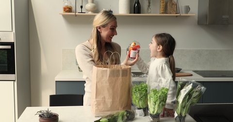 Little girl helps to mom unpack delivered vegetables, gets out from paper bag lettuce leaves, fresh clean paprika. Clients of on-line supermarket services, healthy lifestyle, online shopping concept