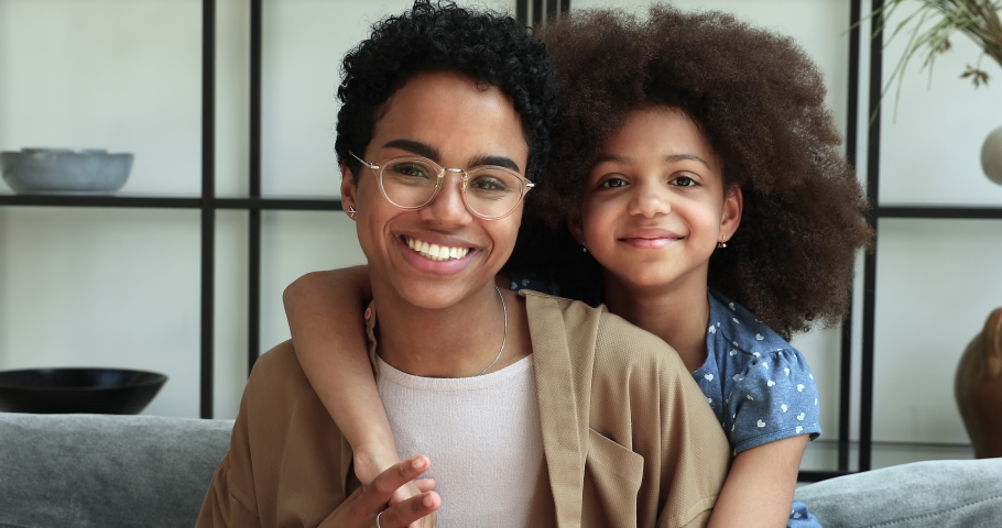 Little African girl piggyback young mom smile look at camera. Pretty curly haired 10s daughter cuddling her older sister or mum express love, feeling affection pose at cam. Mother Day, bonding concept | Shutterstock HD Video #1085053426