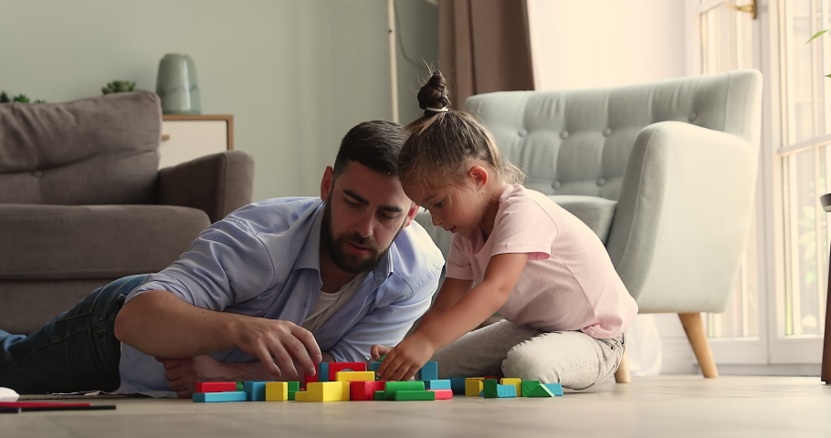 Millennial dad male babysitter play colorful cubes at cozy living room with little child daughter. Bonding single father small girl kid having fun spending time for constructing toy city on warm floor Royalty-Free Stock Footage #1085053522