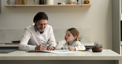 Young father teach little cute daughter to draw pictures in sketchbook, family painting with colored pencil, sit in cozy kitchen. Favourite hobby, children development, creativity, modern home concept