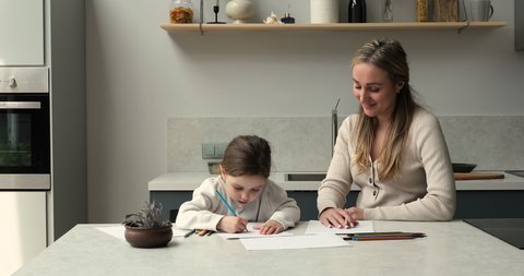 Young woman, little girl sit in kitchen painting pictures in sketchbook. Loving mom and cute daughter enjoy favourite pastime, holds colored pencils absorbed in creative hobby. Family leisure concept