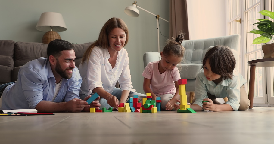Smiling happy parents with small daughter son gather together on warm heated floor play creative game. Foster mom dad two adopted kids construct fantasy buildings from wood blocks at cozy living room Royalty-Free Stock Footage #1085053831