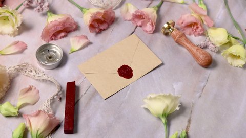 Hands taking wax sealed envelope from a marble table near pink flowers close up 