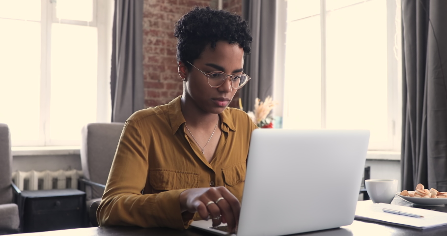 Female freelancer, successful motivated employee, secretary portrait, modern wireless tech usage concept. Happy office worker African woman sit at desk texting on laptop keyboard smile look at camera Royalty-Free Stock Footage #1085056160