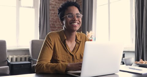 Female freelancer, successful motivated employee, secretary portrait, modern wireless tech usage concept. Happy office worker African woman sit at desk texting on laptop keyboard smile look at camera