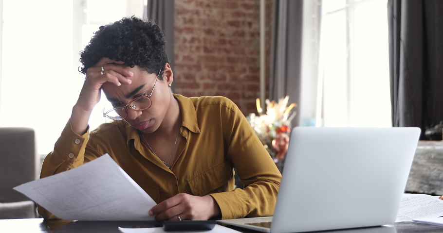 Bad-tempered African woman sit at desk do accounting job or manage personal finances, reviewing bills feels upset due huge taxes, sum need to pay, experiences lack of money, crisis, bankruptcy concept | Shutterstock HD Video #1085057339