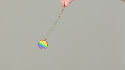 Rainbow colored pendant on chain sways in female hand of hypnotist medium during hypnosis session.