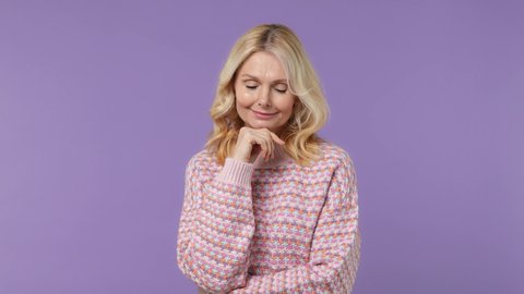 Pensive dreamful thoughtful elderly blonde woman lady 40s years old wears warm shirt look around think dream put hand prop up on chin isolated on plain pastel light purple background studio portrait