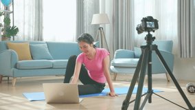Asian Woman In Sportswear Is Sitting On The Floor Using A Laptop And Shoots Video On Camera At Home In The Living Room
