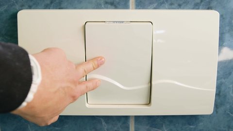 Male hand presses toilet flush button.