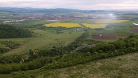 Aerial video over a countryside area with a farm with rape fields in the background. Footage was shot from a drone while flying forward above the Red Ravine in Romania, tilting the camera down.