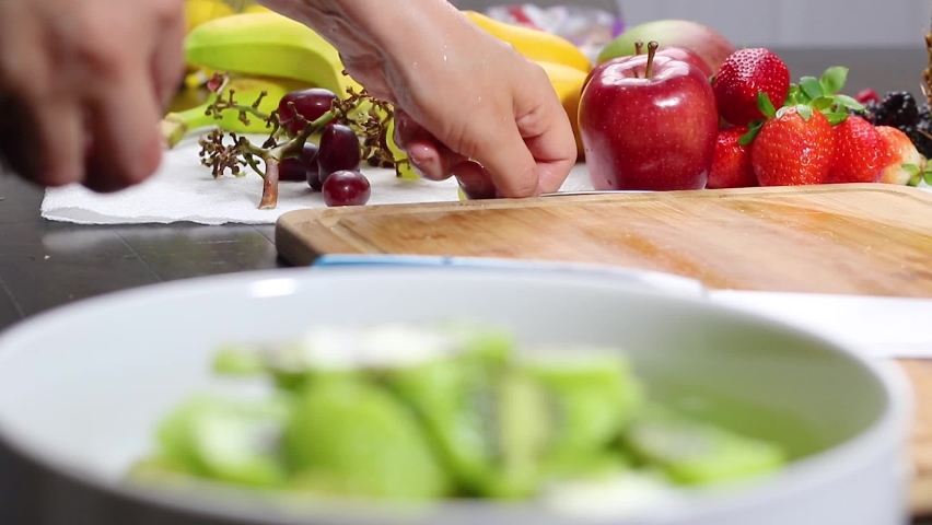 Delicious mixed fruits salad preparation and cutting in a large white bowl with extra fruits in the background. | Shutterstock HD Video #1085081840
