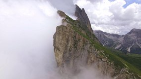 Rotating drone footage of seceda mountain in dolomites covered in clouds. Orbit shot of cloudy rocks. Scenic cloud covered landscape. Drone flying out of clouds and reveal epic view on dolomites. 