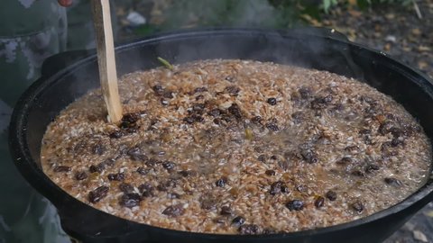 Uzbek man prepares national pilaf in a large cauldron in the open air. Pierces with a wooden stick for better penetration