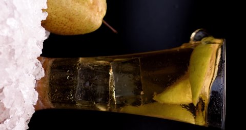 Cold pear juice in a glass moves on the table and is poured from the glass onto the ice. Pear near glass in wooden board with white background. Slow motion, filmed on high speed cinema camera, 4K.